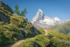 Europaweg trail leads the eye trough lush green meadows to the distant Matterhorn